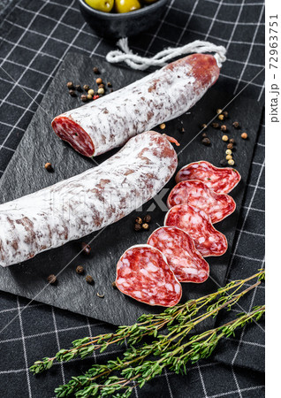 Fuet Salami cut in slices and Rosemary. Traditional Spanish sausage. Black background. Top view Fuet Salami cut in slices and Rosemary. Traditional Spanish sausage. Black background. Top view 72963751