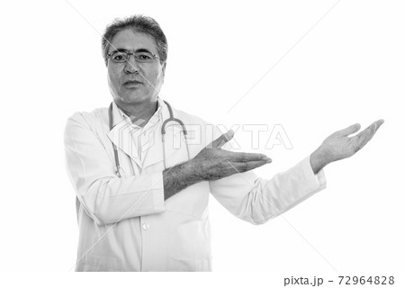 Studio shot of senior Persian man doctor showing something Studio shot of senior Persian man doctor showing something 72964828