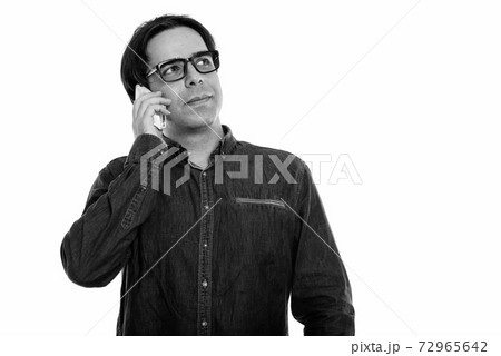 Studio shot of young Persian man talking on mobile phone while thinking Studio shot of young Persian man talking on mobile phone while thinking 72965642