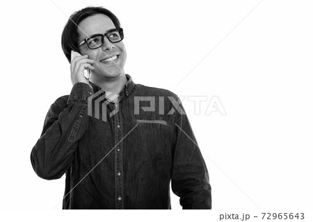 Studio shot of young happy Persian man smiling and talking on mobile phone while thinking 72965643