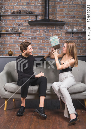 Young man gives christmas gift to his girlfriend. Happy couple of lovers at christmas eve sitting on couch in living room. New year celebration Young man gives christmas gift to his girlfriend. Happy couple of lovers at christmas eve sitting on couch in living room. New year celebration 72966281