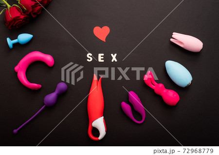The inscription sex is a heart of roses and a collection of vibrators on a black background. Sex toys of various shapes. Assortment of sex shop 72968779
