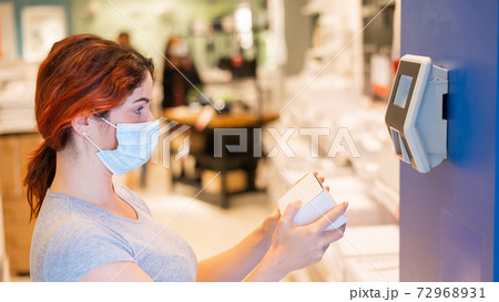 A woman in a medical mask scans the price of an item in a store. An electronic price checker on the wall in a hypermarket A woman in a medical mask scans the price of an item in a store. An electronic price checker on the wall in a hypermarket 72968931