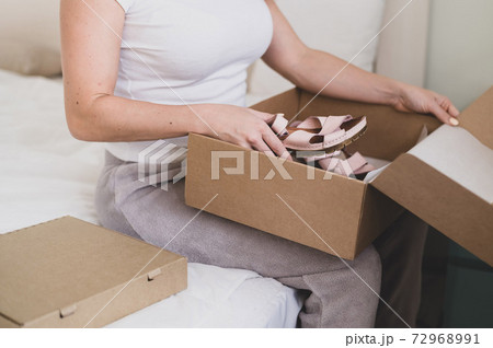 Happy woman unpacks online shopping for shoes. The girl received the package and opens it while sitting in the bedroom Happy woman unpacks online shopping for shoes. The girl received the package and opens it while sitting in the bedroom 72968991