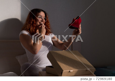 Joyful woman opens ordered shoes while sitting in bed. Online shopping concept with home delivery 72969180
