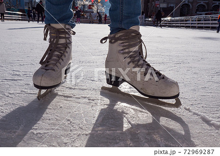 Feet in skates. Public ice-skating rink, pair of skates, scratched ice, sunny day in the winter. Girl skating on ice rink. Close-up photo. Feet in skates. Public ice-skating rink, pair of skates, scratched ice, sunny day in the winter. Girl skating on ice rink. Close-up photo. 72969287