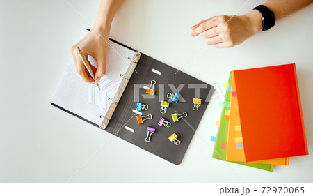 a woman makes a note in a notebook with scattered clips. Nearby is a stack of colored notebooks with bookmarks a woman makes a note in a notebook with scattered clips. Nearby is a stack of colored notebooks with bookmarks 72970065