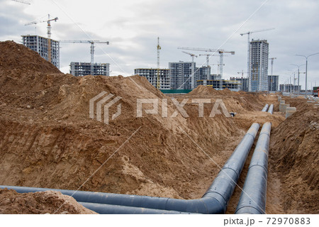 Laying heating pipes in a trench at construction site.  72970883