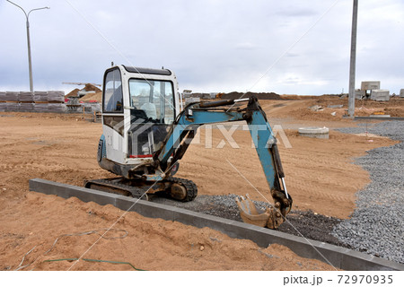 Mini excavator digg trench to lay cables concrete curbs and paving slabs at construction site.  72970935
