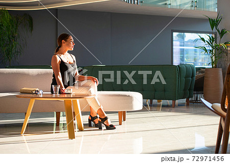 Young adult woman sitting on white sofa in light modern interior of hotel reception, office building hall, waiting area background 72971456