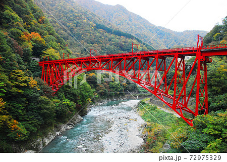 黒部峡谷入り口 宇奈月の赤い鉄橋と紅葉の写真素材