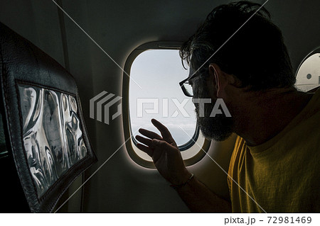 Beard hipster modern man travel on airplane looking outside the window - concept of people fly and use flight transport to move and discover the world or work in new places Beard hipster modern man travel on airplane looking outside the window - concept of people fly and use flight transport to move and discover the world or work in new places 72981469