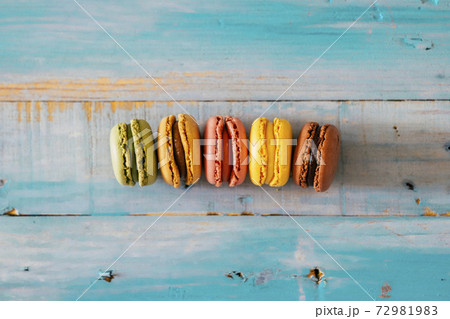 Coloured macarones biscuits on a blue wooden table background - concept of bakery and party lifestyle with sweet snacks - food decorations viewed from above with creak and chocolate Coloured macarones biscuits on a blue wooden table background - concept of bakery and party lifestyle with sweet snacks - food decorations viewed from above with creak and chocolate 72981983