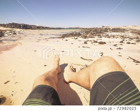 Summer vacation at the beach concept with alternative point of view of man legs and sand - relax and enjoy the ocean outdoor for people 72982025