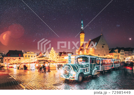 Tallinn, Estonia. Beautiful Train For Sightseeing Near Traditional Christmas Market On Town Hall Square. Christmas Tree And Trading Houses. Famous Landmark. Altered Night Sky 72985449