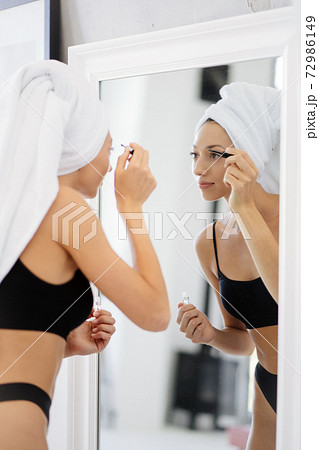 Woman in lingerie and a head towel applies makeup 72986149