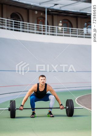 Young guy raises the bar in the stadium, outdoor workout Young guy raises the bar in the stadium, outdoor workout 72986685