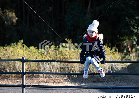 冬の公園で柵に座る女の子 冬の公園で柵に座る女の子 72989117