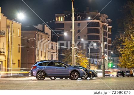 Blue car parked on brightly illuminated city street at night. 72990879