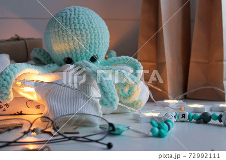 Blue knitted octopus toy sits on a white sweater on the table Blue knitted octopus toy sits on a white sweater on the table 72992111