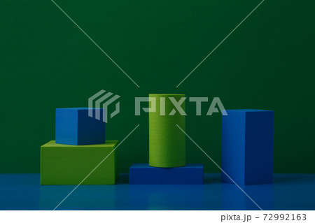 Still life with green and blue geometric figures on blue table against green background with space for text Still life with green and blue geometric figures on blue table against green background with space for text 72992163
