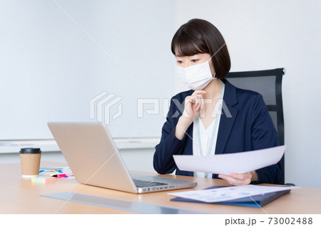オフィスでマスクをして仕事をする女性 オフィスでマスクをして仕事をする女性 73002488