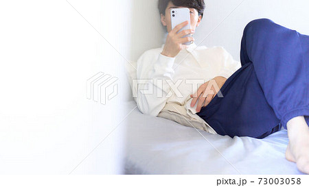 ベッドの上でスマホを触る若い男性 ベッドの上でスマホを触る若い男性 73003058