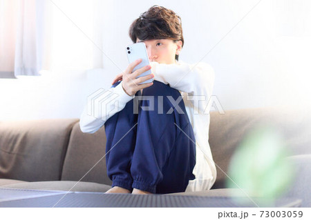 ソファーの上でスマホをいじる若い男性 ソファーの上でスマホをいじる若い男性 73003059