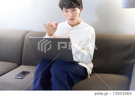 ソファーでPCを使う若い男性 73003060