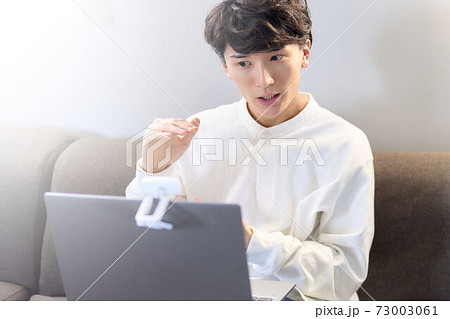 ソファーでビデオ通話をしている若い男性 ソファーでビデオ通話をしている若い男性 73003061