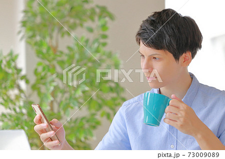 コーヒーカップを持ちスマホを見るビジネスマン 73009089