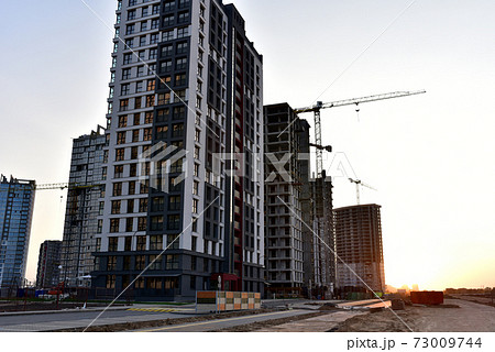 View on the large construction site with tower cranes and buildings on sunset background. View on the large construction site with tower cranes and buildings on sunset background. 73009744
