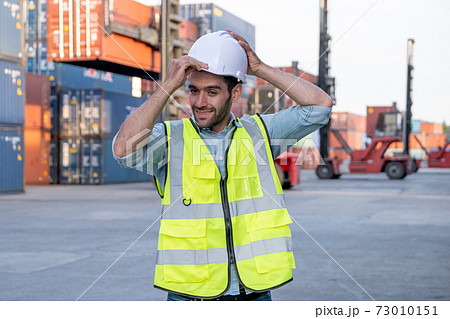 Foreman engineer or cargo container worker hold hardhat and stand in front of cranes 73010151