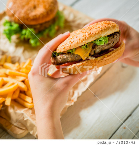 Hands and delicious burger with meat, french fries, sauce on the wooden table Hands and delicious burger with meat, french fries, sauce on the wooden table 73010743