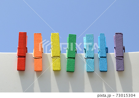 Seven wooden multi-colored clothespins, painted in the colors of the rainbow, against the blue sky 73015304