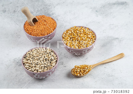 Raw corns, beans and red lentil in purple bowls 73018392