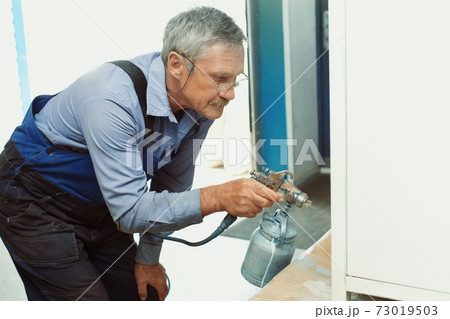 Painting of metal products. An elderly man paints a Cabinet with a compressor 73019503