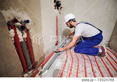 Male worker installing underfloor heating system in apartment. 73024708