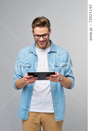 Happy young man wearing jeans shirt standing and using tablet over studio grey background 73025142