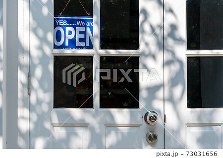Blue open sign hanging on the white entrance door of a business office 73031656
