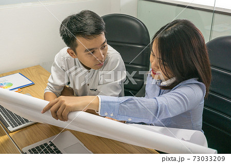 Two Asian office employee discuss about information on paper 73033209