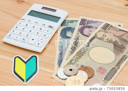電卓の隣に置かれた紙幣と硬貨 73033850