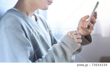 部屋でスマホを操作する男性の手元 73034339
