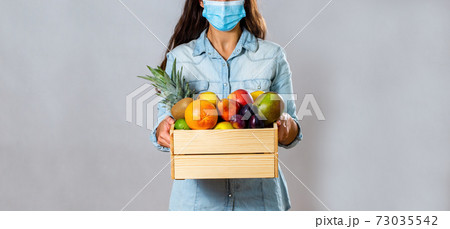 Woman with box full of fresh fruit protecting with face mask 73035542