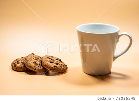 Close up white mug of milk and three dark chocolate chip cookies 73036549