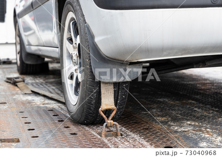 Close-up of car wheel tied with safety harness on flatbed tow truck 73040968