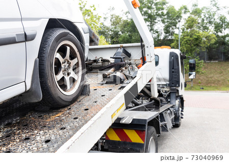 Cable attached to broken down car being pulled onto tow truck 73040969