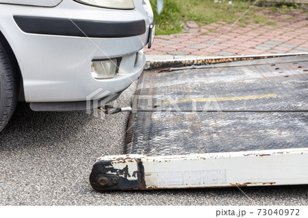Cable attached to broken down car being pulled onto tow truck 73040972