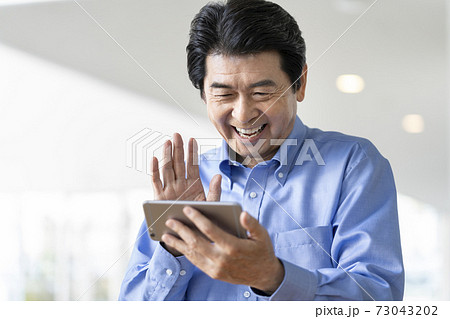 スマートフォンの画面に向かって手を振る笑顔のシニア男性 73043202