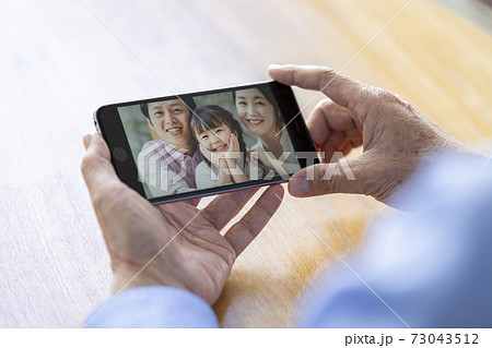 家族とビデオチャット　イメージ　スマートフォンを持つシニア男性の手元 73043512
